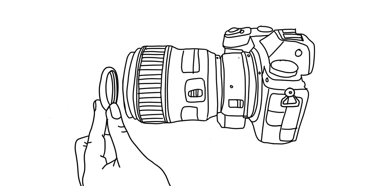 Imaginea prezintă un aparat foto cu o mână care ține un inel în fața obiectivului.