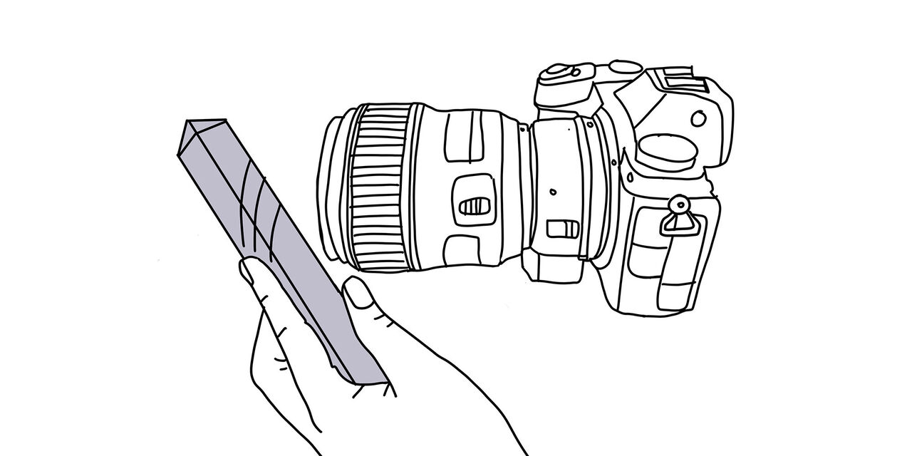 O imagine a unui aparat foto cu o mână care ține o prismă în fața obiectivului.