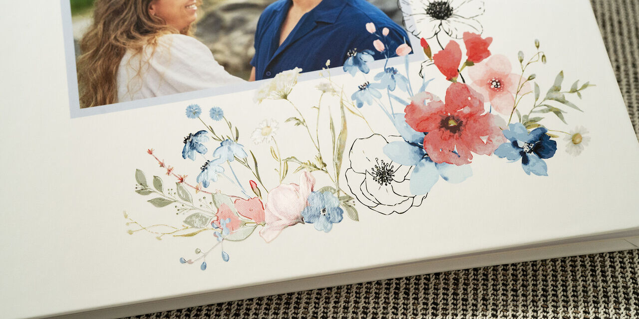 Prim-plan al copertei cărții de oaspeți, cu o fotografie a mirilor. Cartea este decorată elegant, cu un design floral de nuntă și un fundal alb efect de lăcuire.